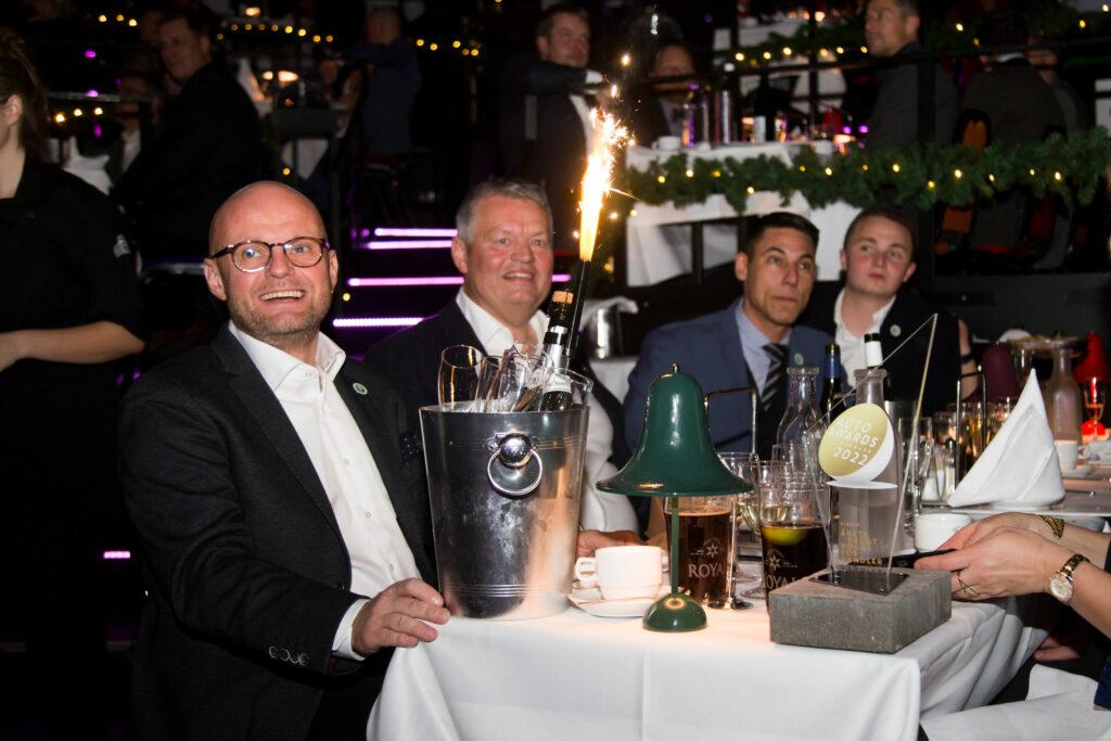 Glad Henrik Bollerslev med champagneflaske og prisen som Årets Brugtvognsforhandler 2022