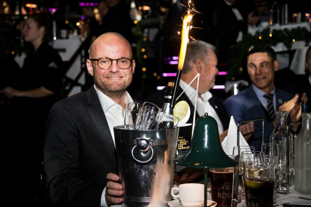 Henrik Bollerslev med champagneflaske og prisen for Årets Brugtvognsforhandler til Autoawards 2022